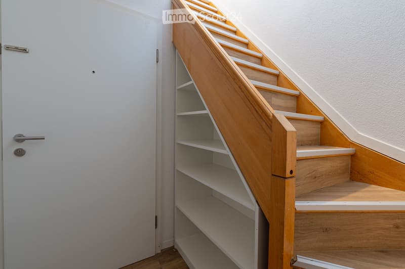 A modern staircase with wooden steps and a built-in storage shelf on one side, adjacent to a white door.