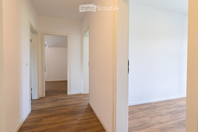 Empty hallway with light-colored walls, wooden flooring, and multiple doors leading to other rooms.