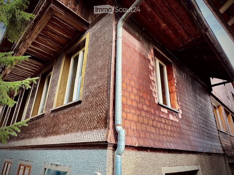 Two-story building with wooden and brick exterior, multiple windows, and a visible downspout.