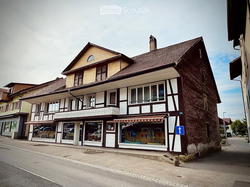 Two-story building with a mix of brick and plaster exterior, multiple windows, and a storefront with awnings and signage.