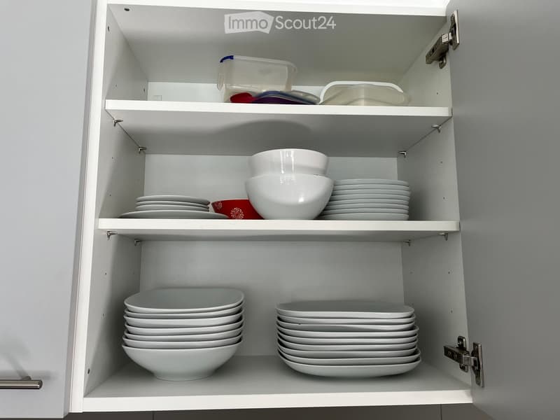 Open kitchen cabinet with neatly arranged white plates and bowls on multiple shelves.