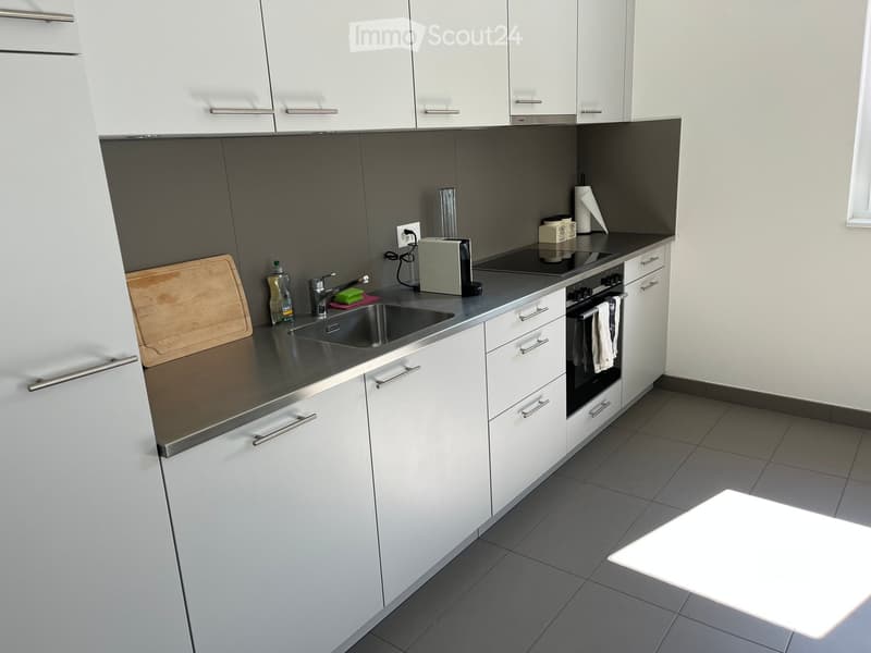 Modern kitchen with white cabinets, stainless steel sink, oven, and countertop items including a cutting board, bottle, and toaster.