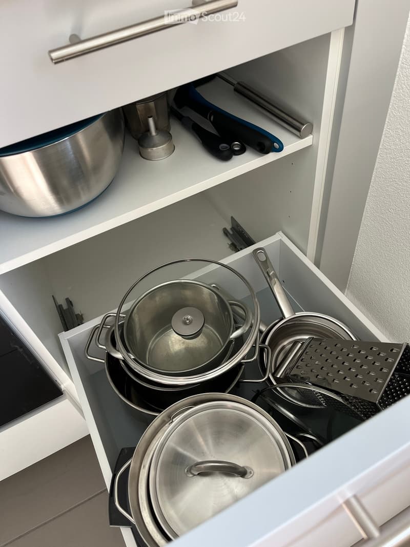 Open kitchen cabinet with neatly organized stainless steel pots, pans, and a grater inside.