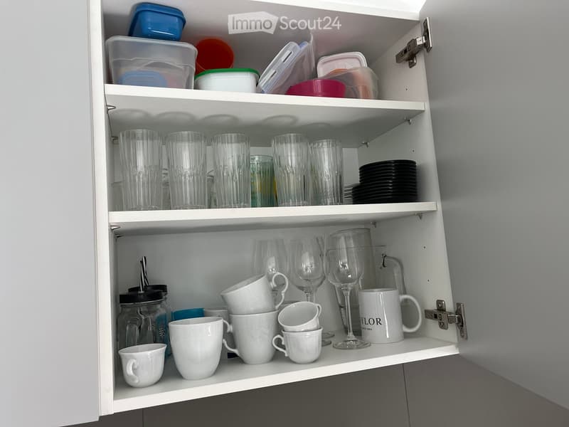 Open kitchen cabinet with neatly arranged glassware, cups, plates, and storage containers on multiple shelves.
