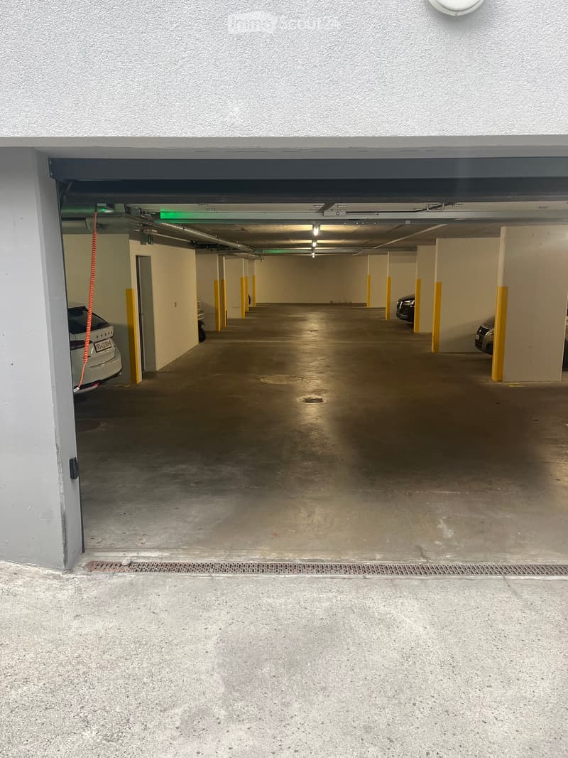 Underground parking area with concrete floors, yellow support pillars, and a few parked cars visible in the background.
