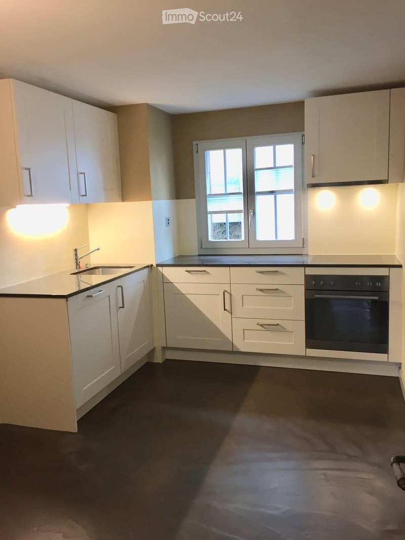 Modern kitchen with white cabinets, dark countertops, and a built-in oven. Features a window above the sink and sleek, contemporary design.