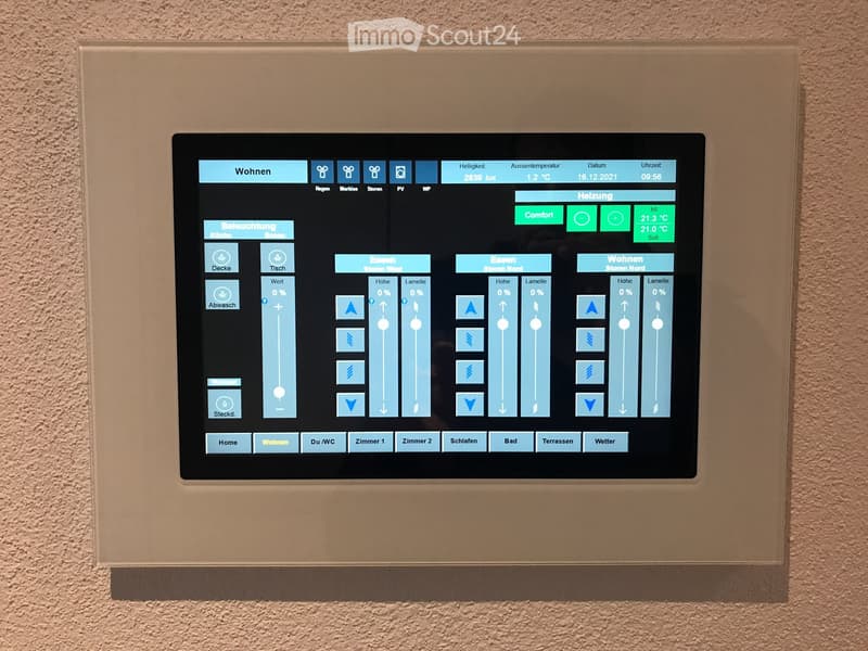 A modern home automation control panel with a touchscreen display showing various room settings, weather data, and control options for lighting, heating, and other systems.