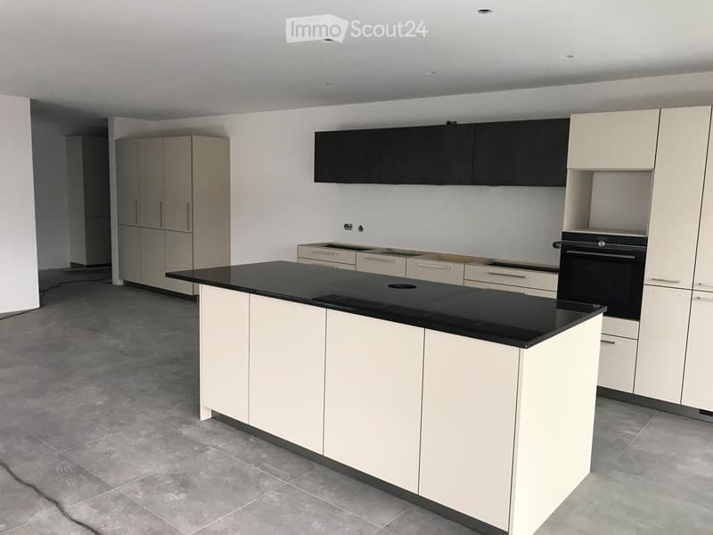 Modern kitchen with white cabinets, black countertop, and built-in oven. Features include a central island and sleek design.