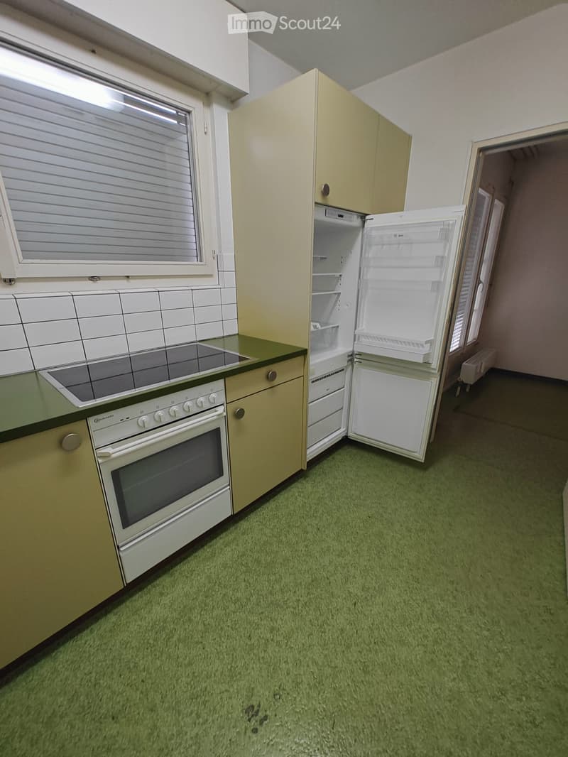 Small kitchen with green carpet, cream-colored cabinets, white refrigerator, and white oven.
