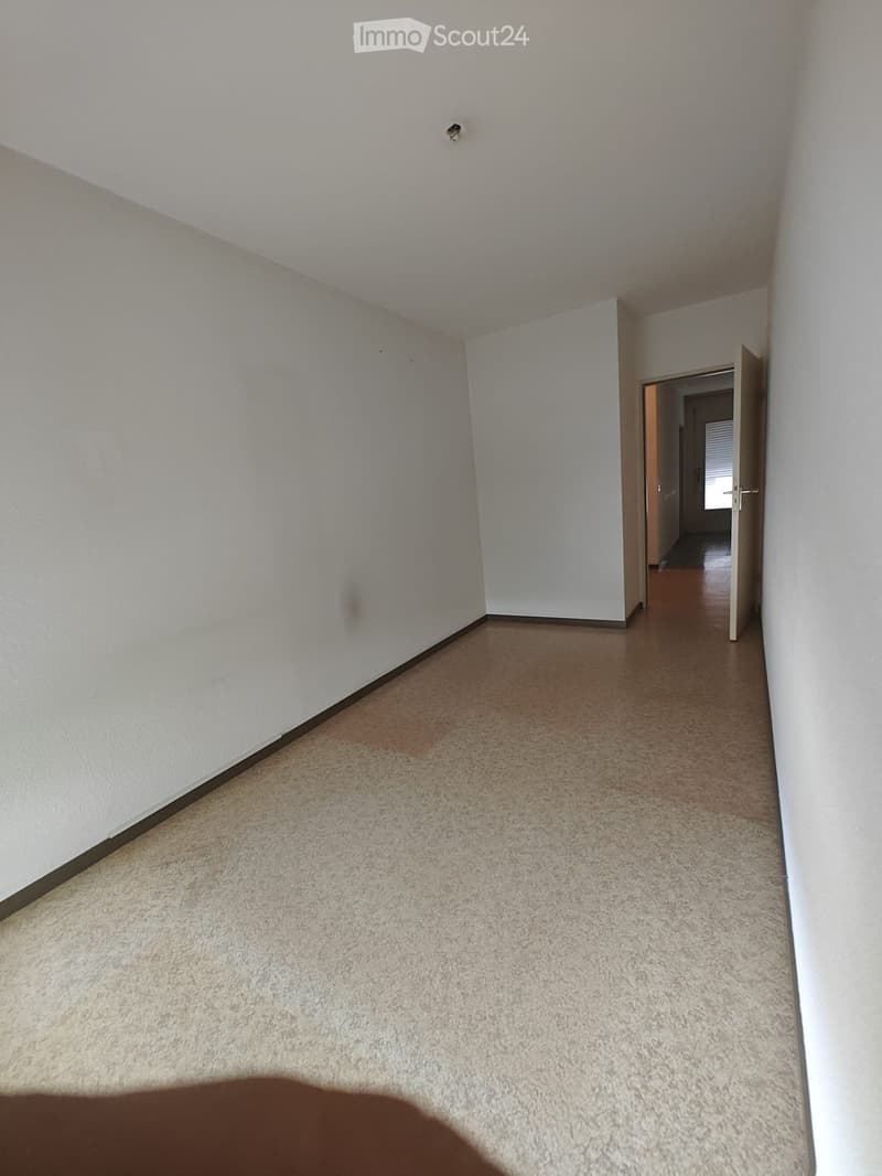 Empty hallway with beige carpet and white walls, featuring an open doorway leading to another room.