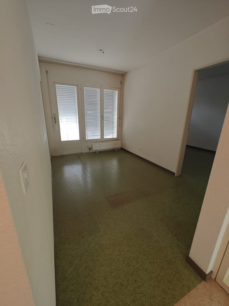 Empty hallway with beige walls, green carpeted floor, and a door with blinds on the left side.