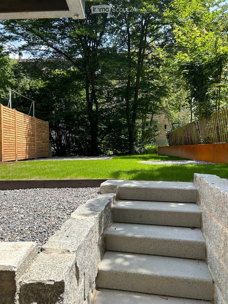 Garden with concrete steps leading up, gravel area, wooden fence, and lush green lawn.