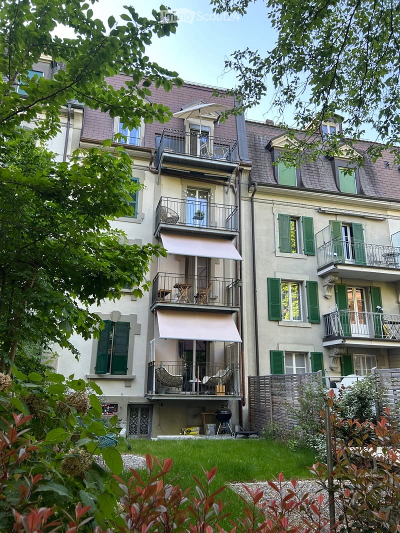 Multi-story residential building with multiple balconies, green shutters, and a well-maintained garden area.