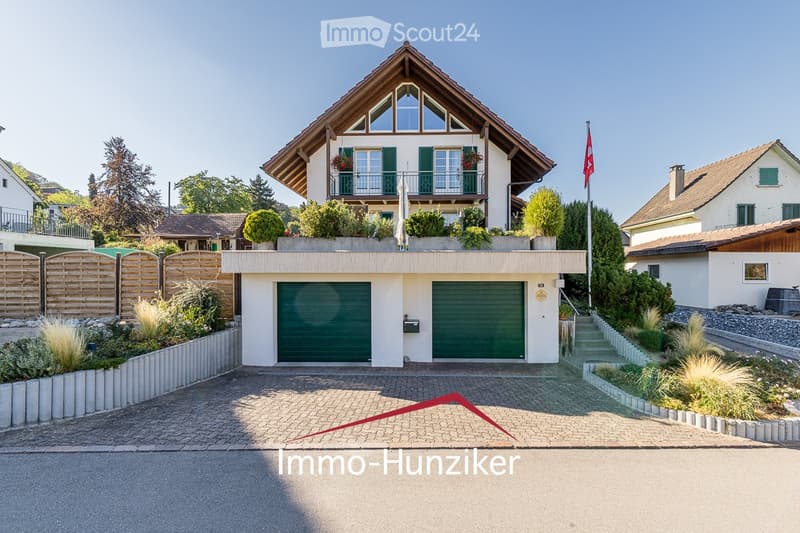 A two-story house with a modern design, featuring a garage, balcony, and well-maintained garden.