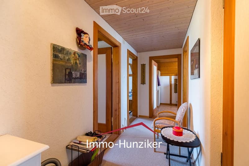Cozy hallway with wooden doors, a small seating area featuring a chair and table, and artwork on the walls.