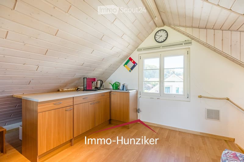 Bright kitchen with wooden cabinets, a central island, and a coffee maker on the counter. The room features wooden flooring and a slanted ceiling with exposed beams.