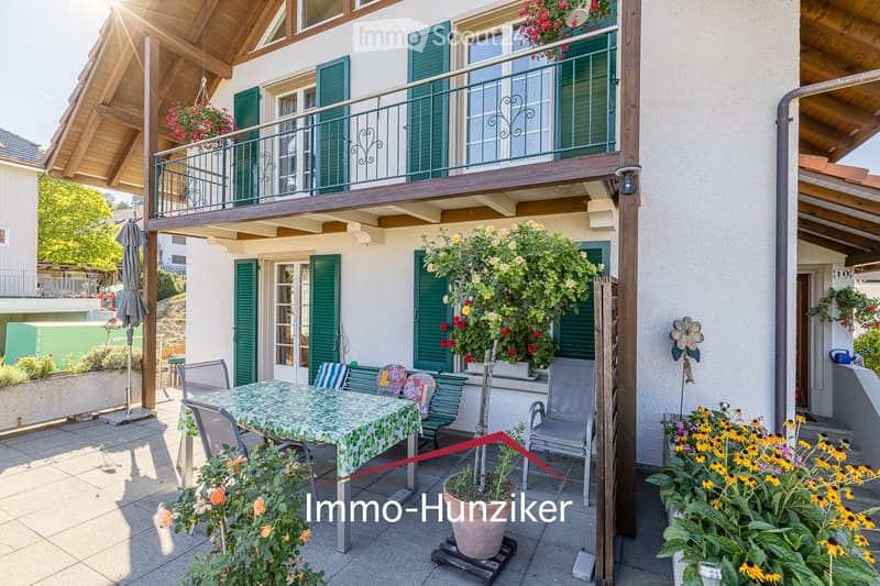 Outdoor patio area with a dining table, chairs, benches, potted plants, and a covered balcony above.