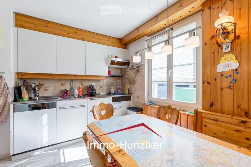 Bright kitchen with white cabinets, wooden accents, and a dining area. Features a dishwasher, oven, refrigerator, and a wooden dining table with chairs.