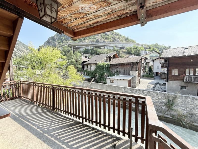 Balcony overlooking a scenic town with traditional wooden houses, a stone wall, and a river below.