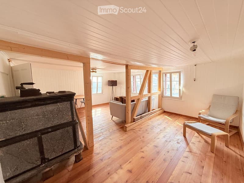 Bright, wooden-floored room with exposed wooden beams, a fireplace, a sofa, chairs, a small table, and a floor lamp.