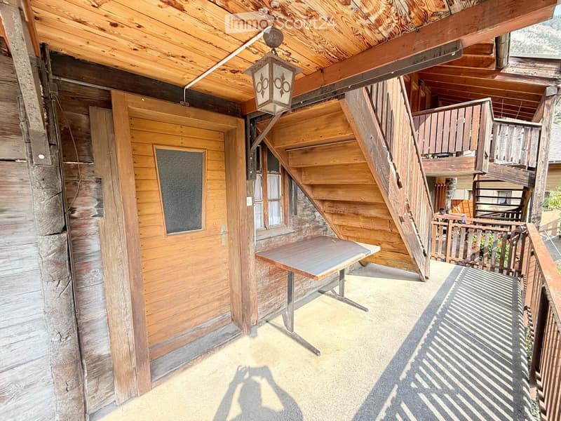 Wooden balcony with a table, wooden railing, and a staircase leading to an upper level.