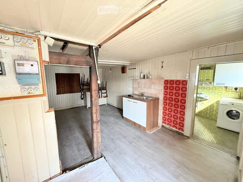 The image shows a partially furnished room with a kitchen area, a sink, a washing machine, and a small dining area with a table and chairs.