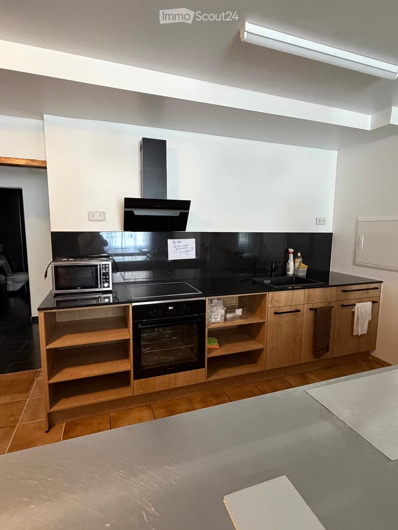 Modern kitchen with white cabinets, wooden shelves, microwave, oven, sink, and a countertop.