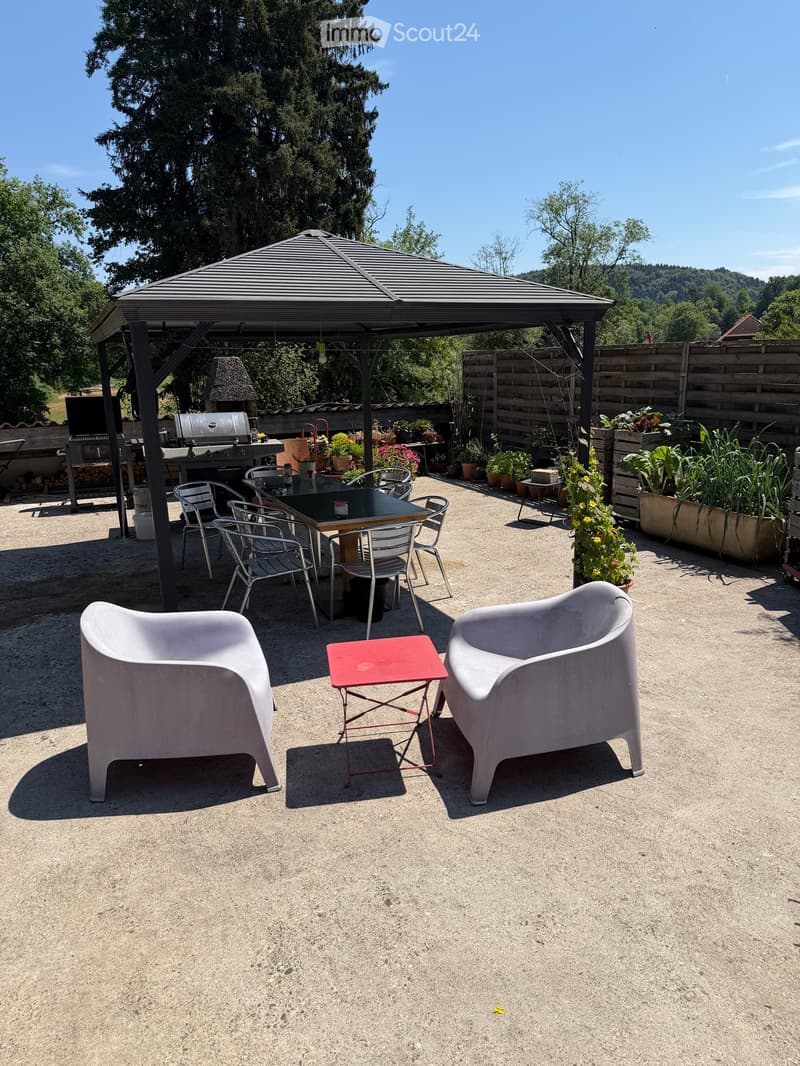 Outdoor patio area with a covered seating area, grill, and garden plants.