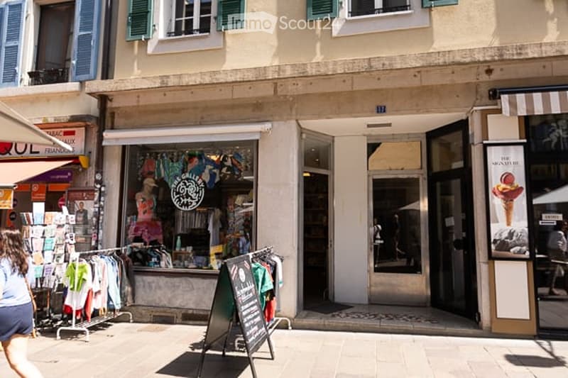 Facade of a multi-story building with shops on the ground floor, including a clothing store and an ice cream shop, with awnings and signage visible.