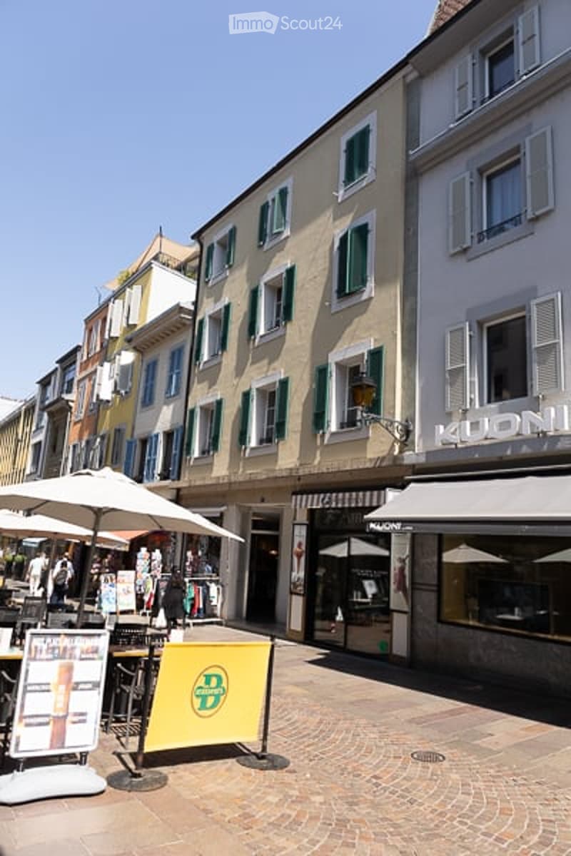 A charming outdoor area with a cobblestone pavement, colorful buildings with shutters, and outdoor seating under umbrellas.