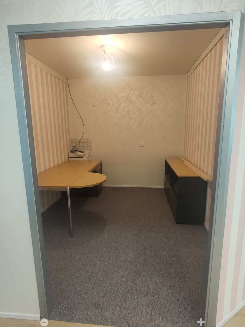 Small furnished room with a desk, cabinet, and carpeted floor.