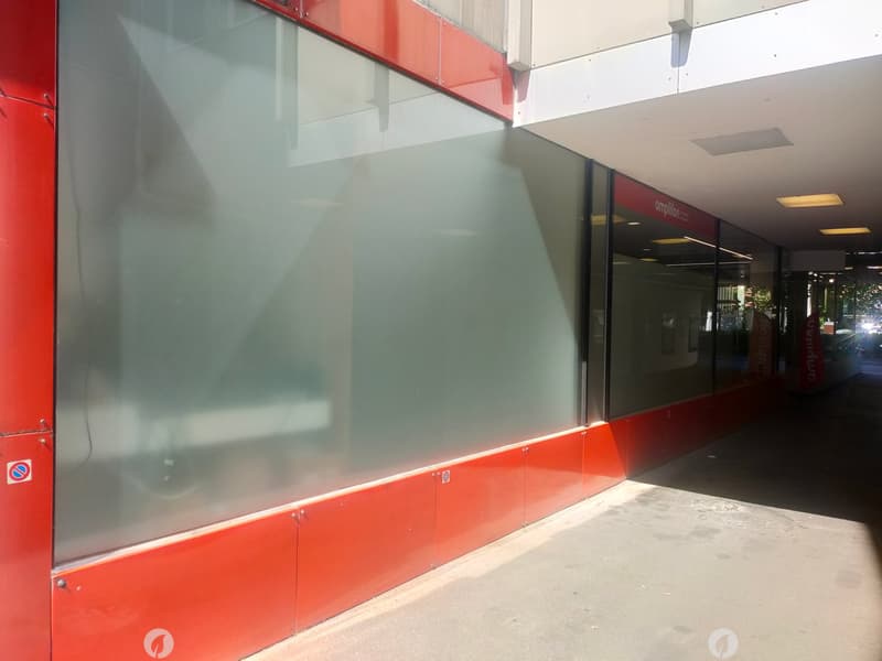 Modern building exterior with large glass windows and red panels, featuring a covered walkway and signage for 'Amplification'.