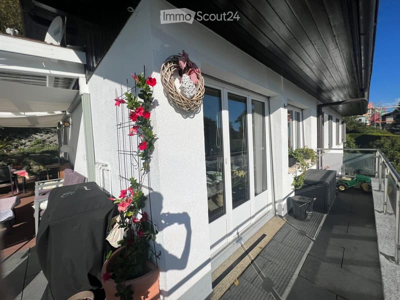 Balcony with a covered area, potted plants, a covered grill, and a decorative wreath on the wall.