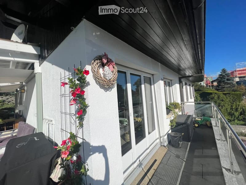 Balcony with a covered grill, a chair, a small table, and a decorative wreath on the wall.