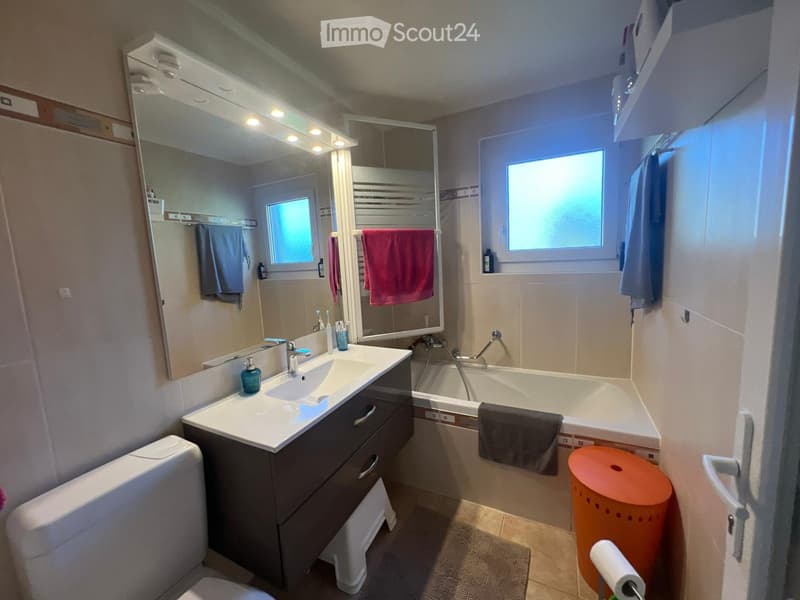 Modern bathroom with a double sink vanity, bathtub, large mirror with built-in lighting, and various towels and toiletries.