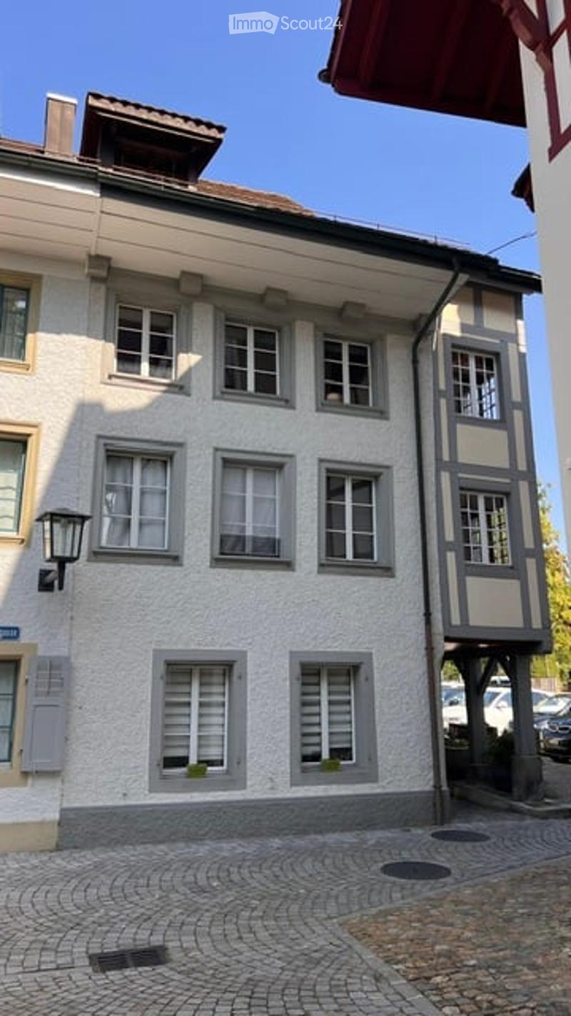 A multi-story residential building with a light-colored facade, multiple windows, and a cobblestone street in front.