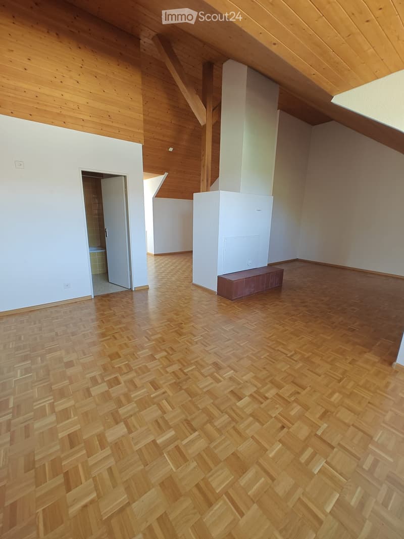 Empty attic room with wooden herringbone flooring, white walls, exposed wooden beams, and a small built-in bench.