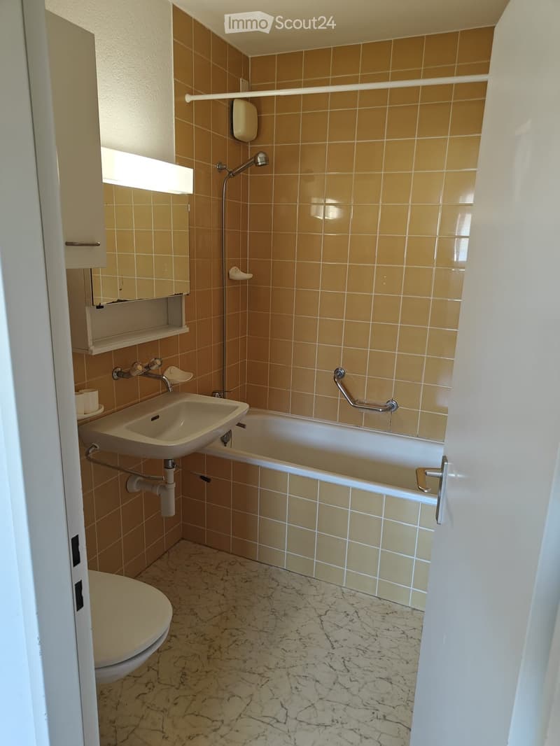 Bathroom with beige tiles, marble flooring, sink, bathtub, toilet, and a small window above the sink.