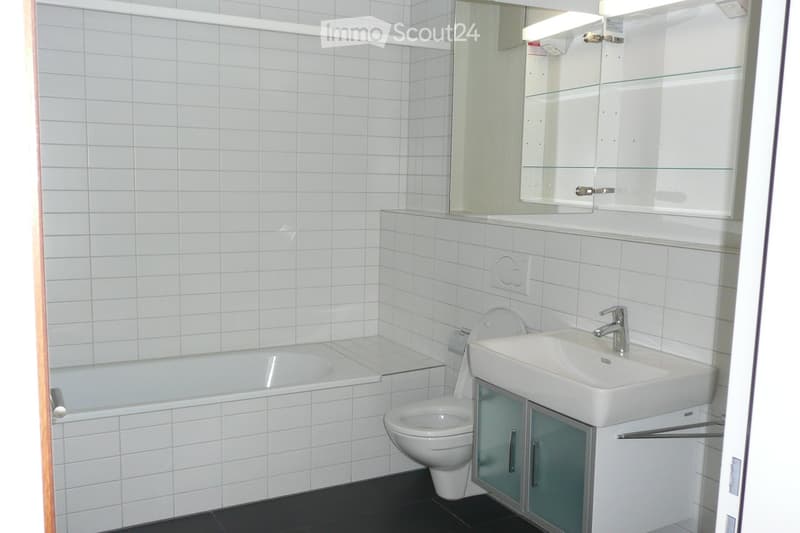 Modern bathroom with white tiled walls, a bathtub, toilet, sink, and a mirrored cabinet.