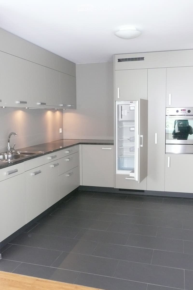 Modern kitchen with grey cabinets, stainless steel appliances, dark tiled floor, and a sink with a faucet.