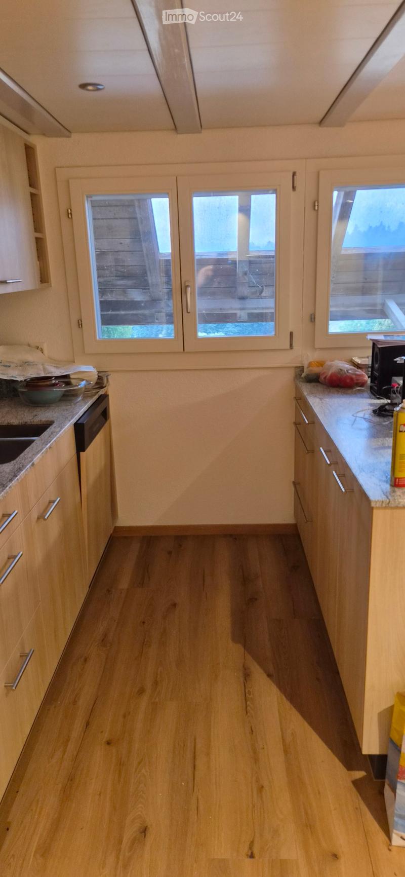 Modern kitchen with light wooden cabinets, granite countertops, and a central island. Features a dishwasher, sink, and various kitchen items on the counters.