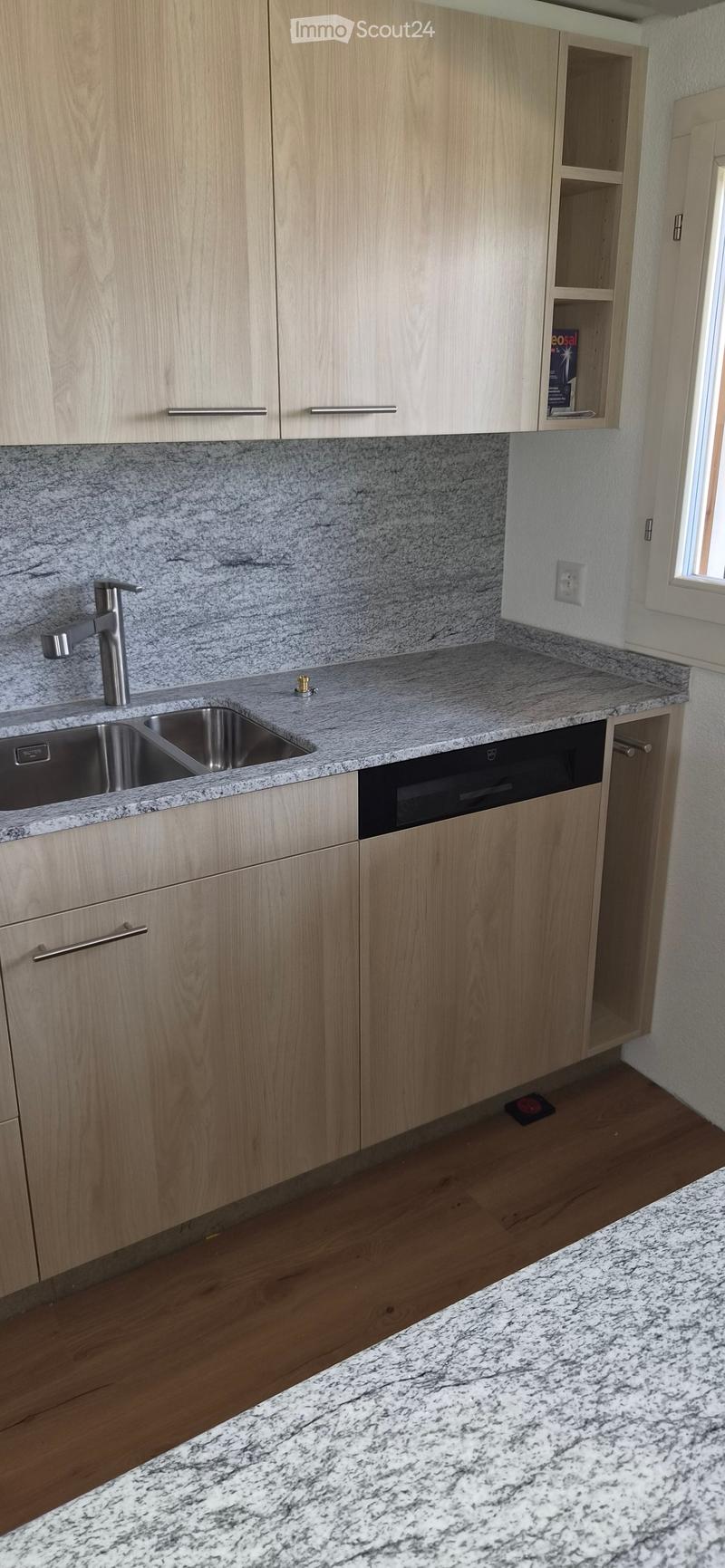 Modern kitchen with light wood cabinets, granite countertops, and a stainless steel sink.