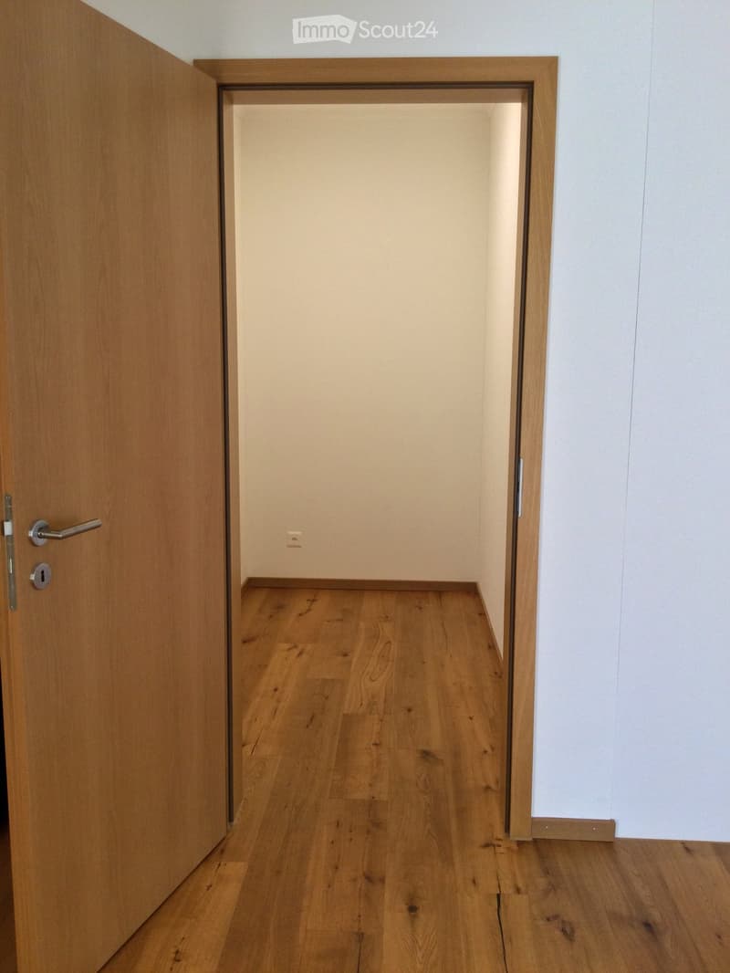 Empty hallway with wooden flooring and white walls, featuring a partially open wooden door on the left and a closed wooden door on the right.
