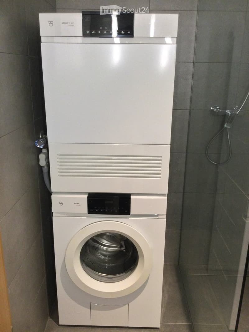 Modern bathroom with a white stacked washing machine and dishwasher unit, glass shower enclosure, and tiled walls.