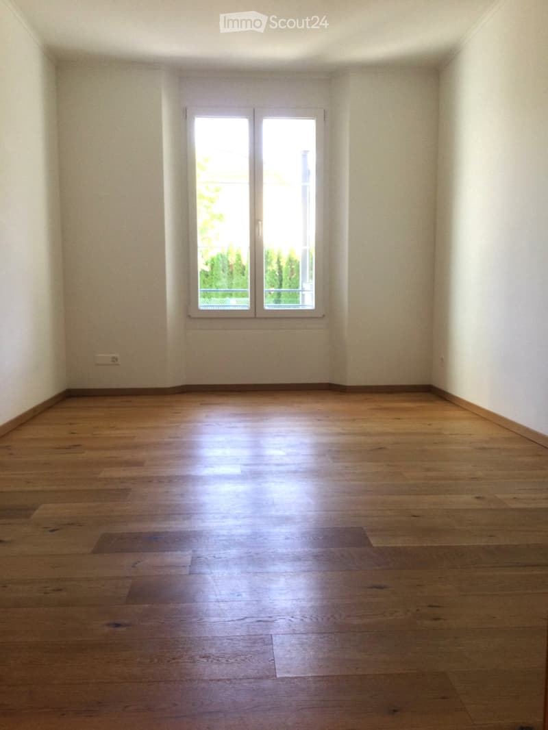 Empty room with wooden flooring and white walls, featuring a large window with double glass panels allowing natural light to enter.