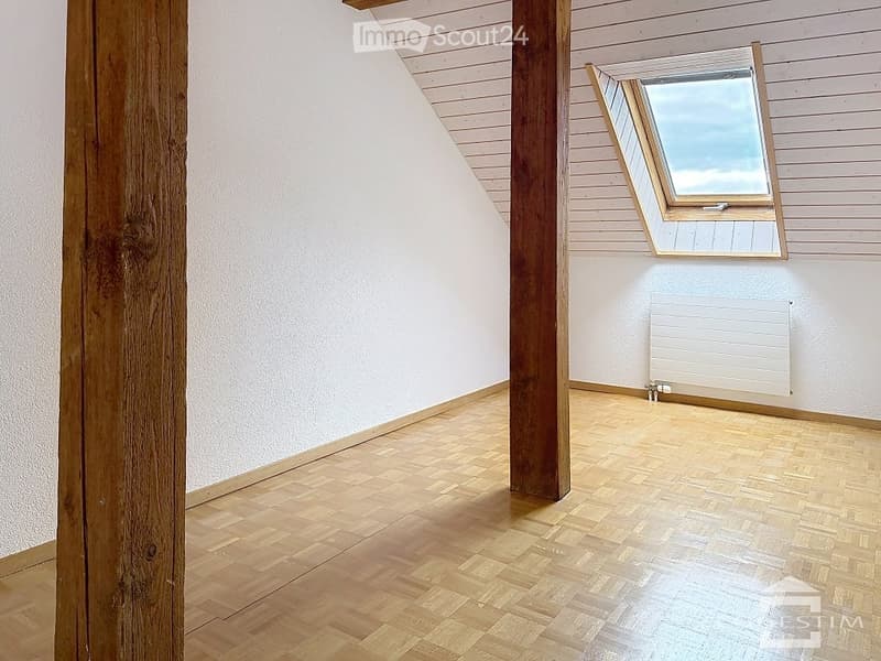 Empty attic room with wooden flooring, white walls, exposed wooden beams, and a skylight window.
