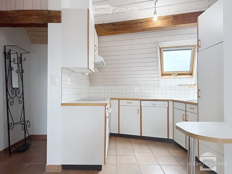 Bright kitchen with white cabinets, tiled walls, and a dishwasher. Features a wooden ceiling and a small window above the sink.