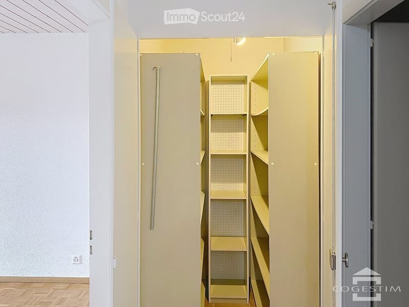 Empty closet with built-in shelves and hanging rod, light-colored wood finish, white walls, wooden floor.