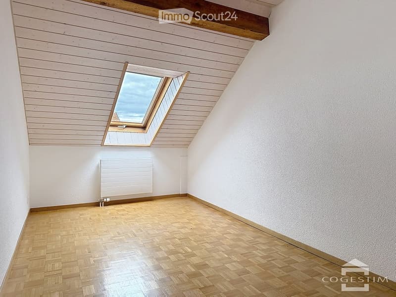 Empty room with wooden flooring, white walls, and skylight windows in the sloped ceiling.