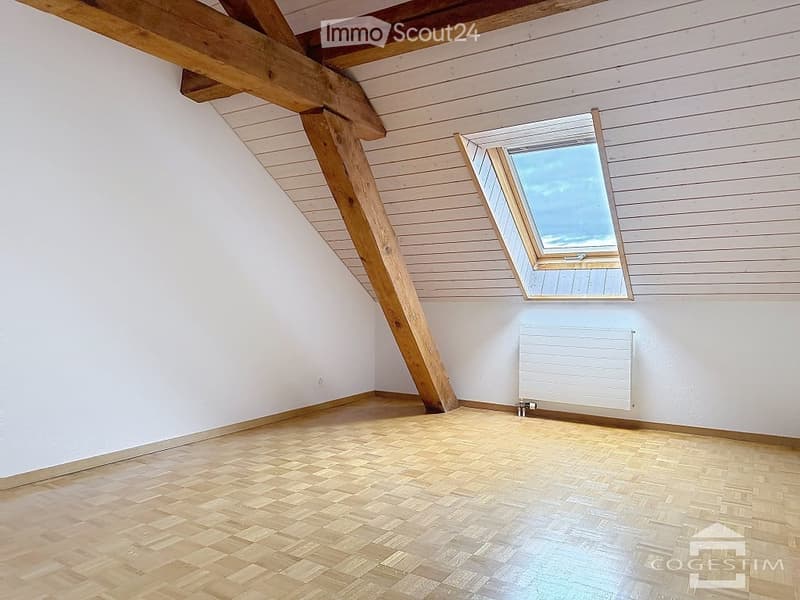 Empty attic room with wooden beams, wooden floor, white walls, and a skylight window.